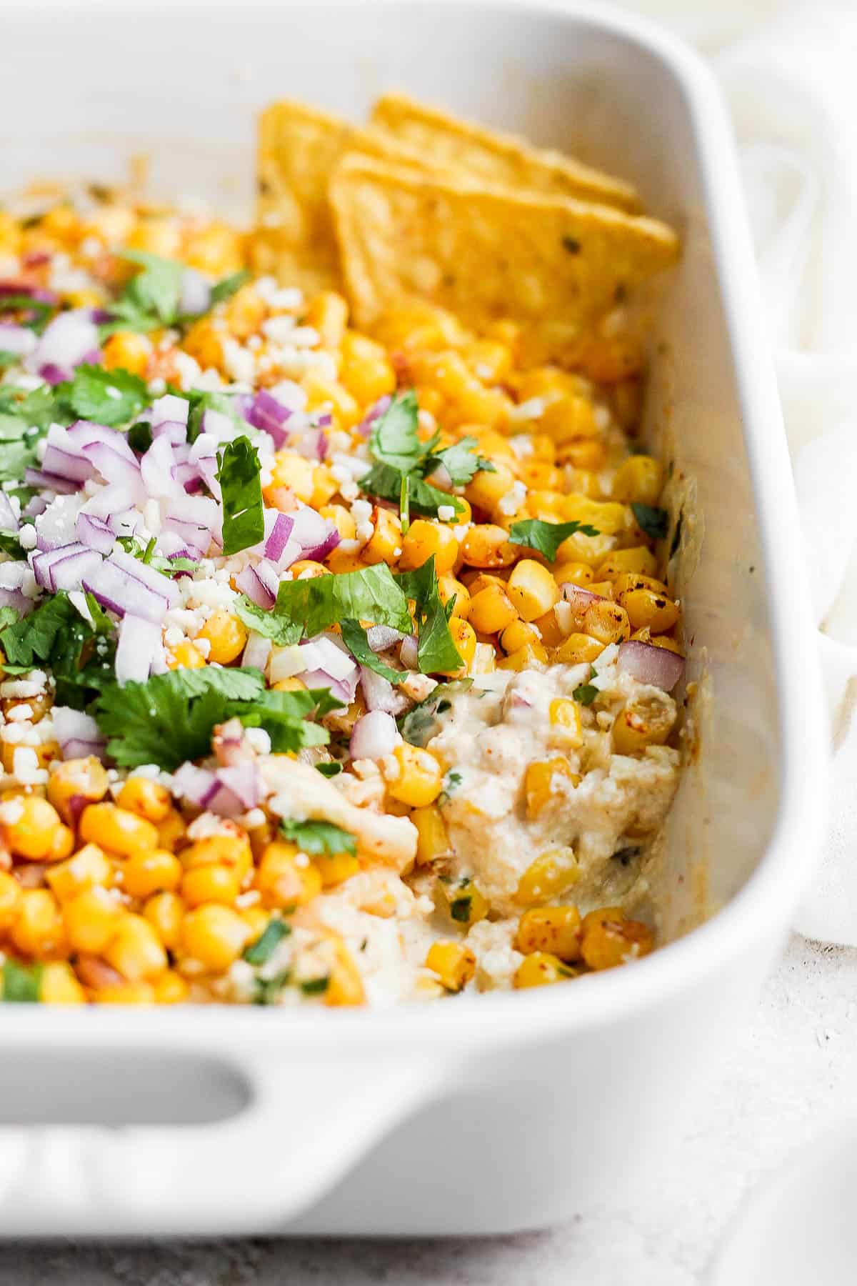 A baking dish with Mexican street corn topped with chopped cilantro and diced red onions.