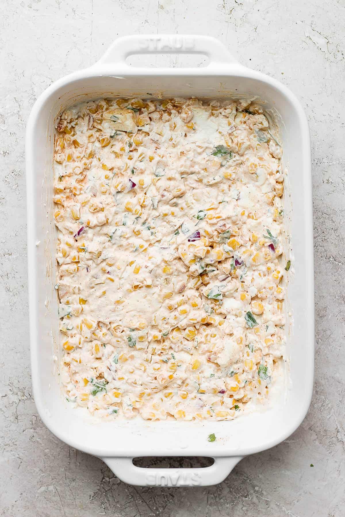 The baking dish with the cream cheese, mayo, and sour cream mixed in with the corn mixture and spread evenly on the bottom of the baking dish.
