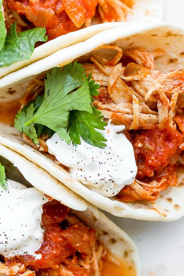 A plate of salsa chicken tacos with sour cream and fresh cilantro.