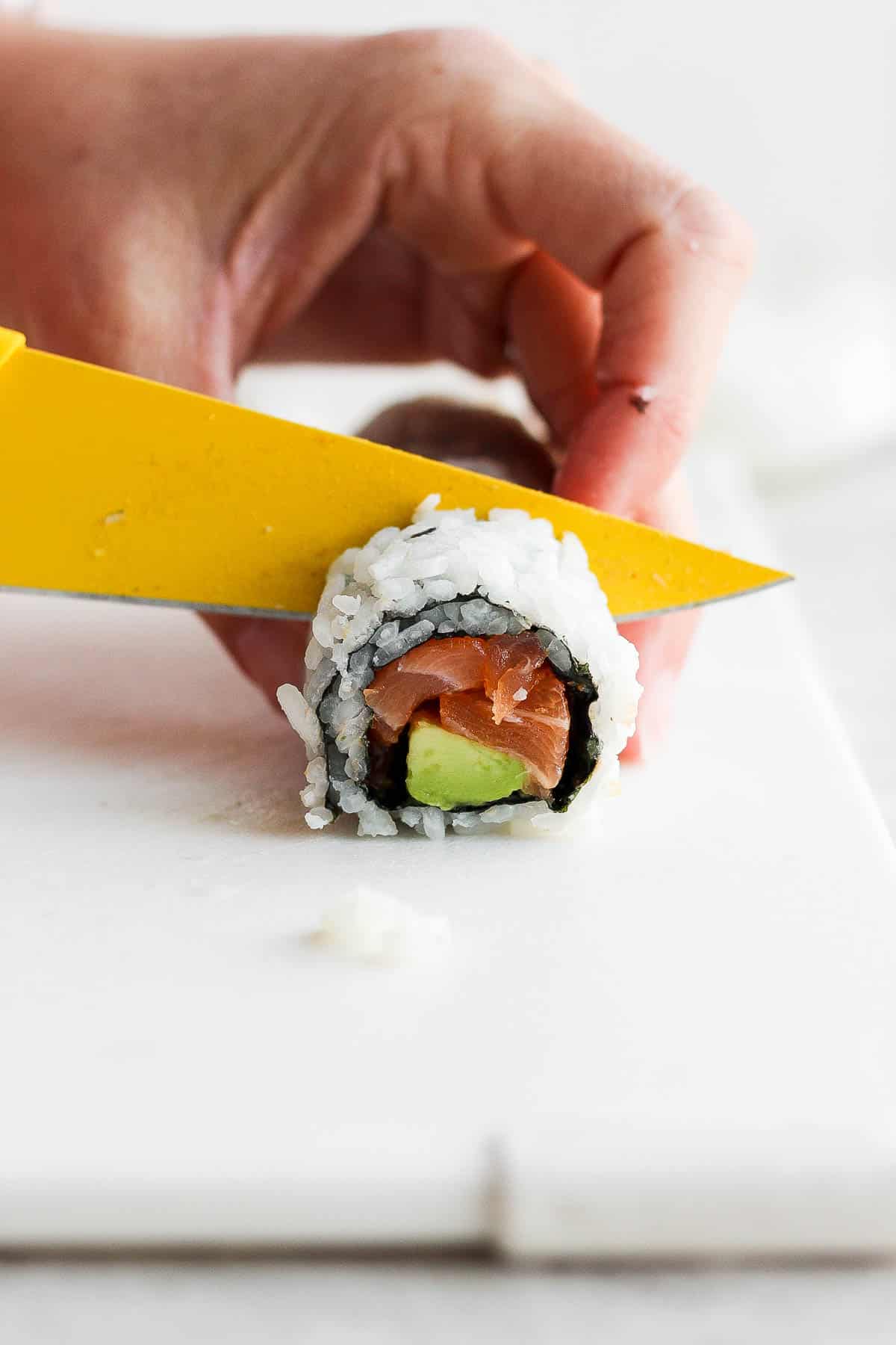 The spicy salmon roll being cut with a sharp knife.