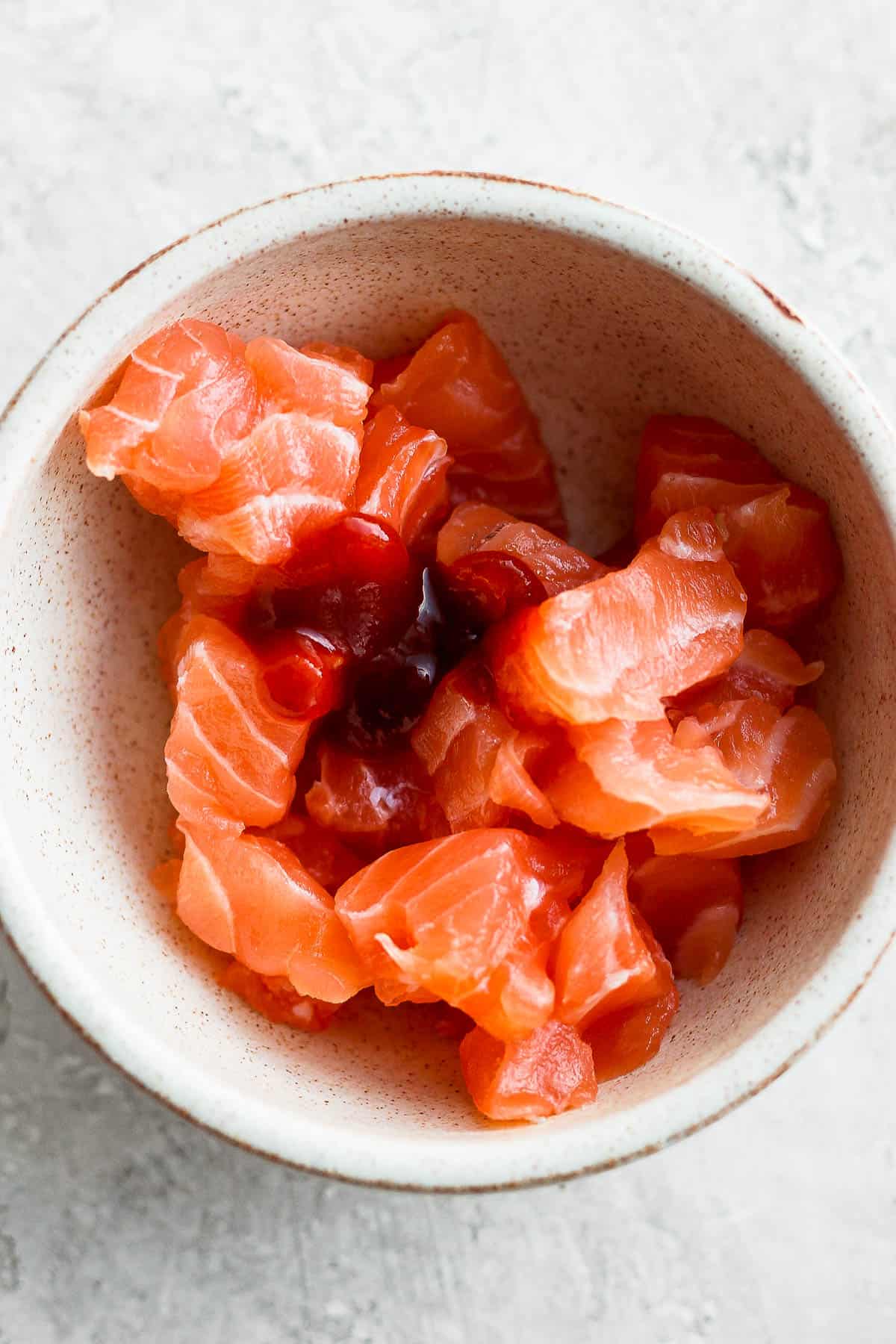 A small bowl of sriracha on chunks of salmon.