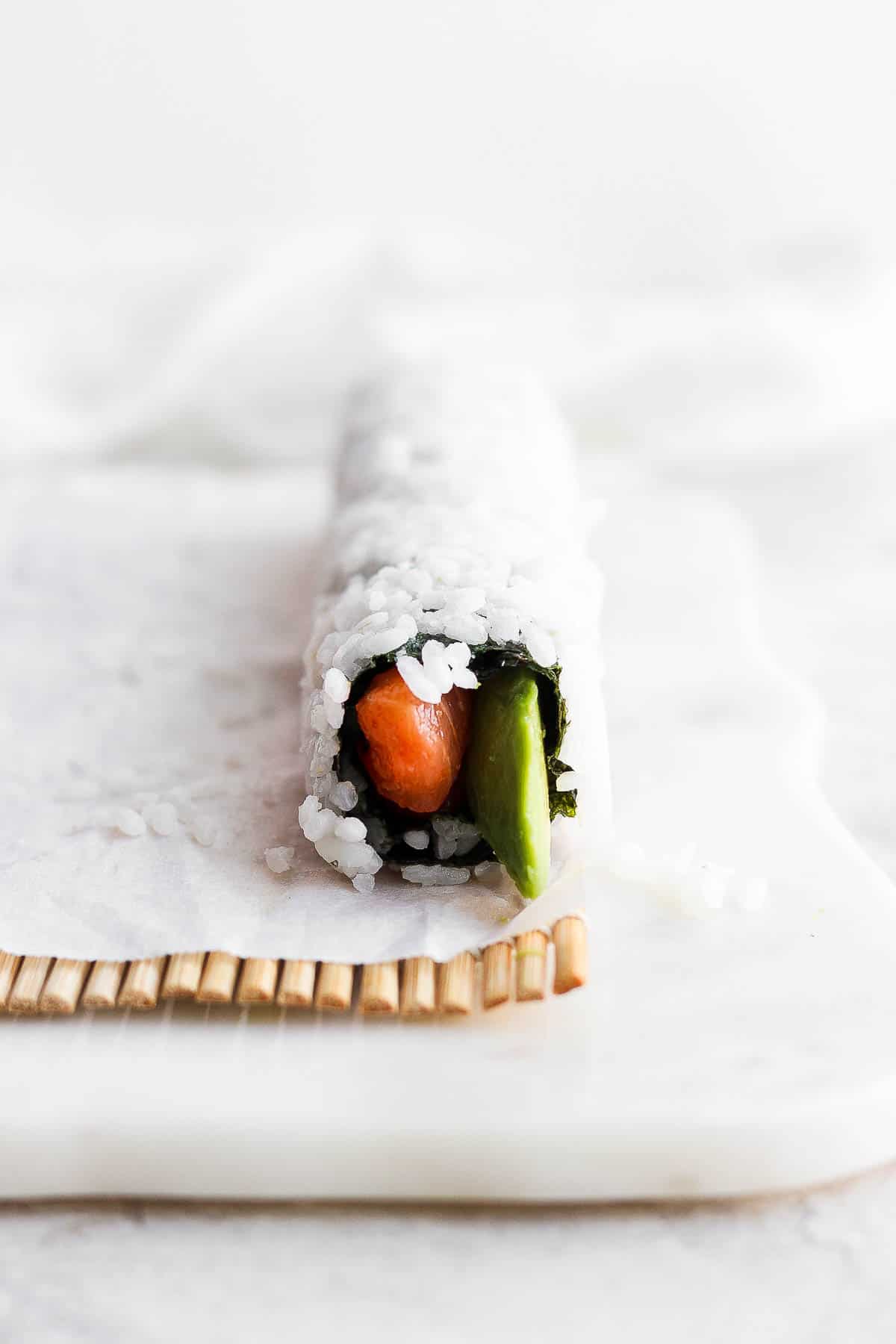 A spicy salmon roll on the parchment-lined bamboo sheet.