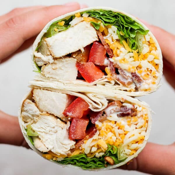 Someone holding a chicken bacon ranch wrap that has been cut in half to show the inside.
