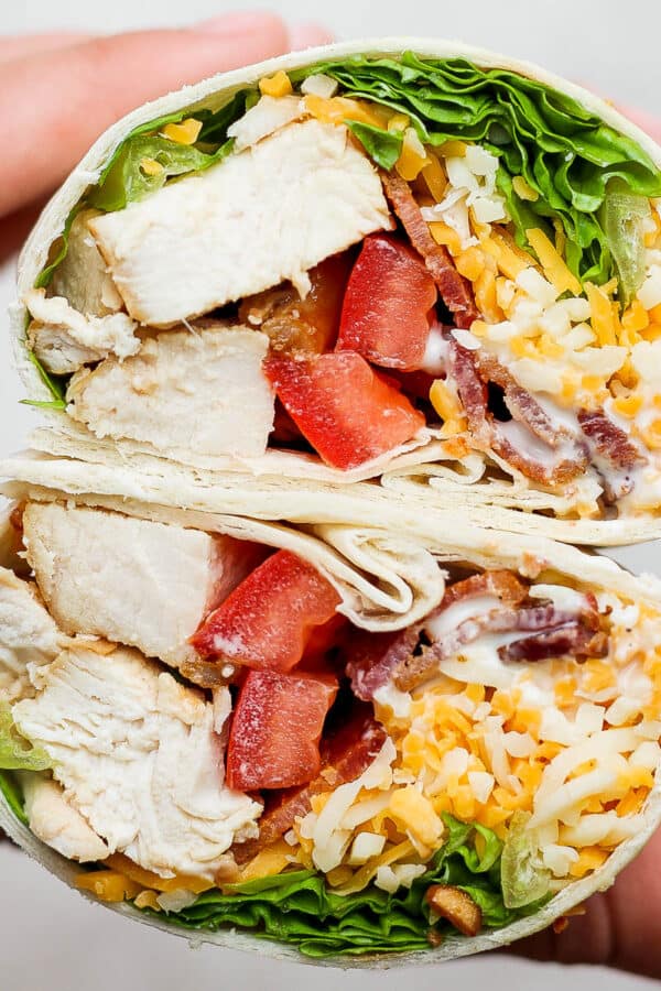 Someone holding a chicken bacon ranch wrap that has been cut in half to show the inside.