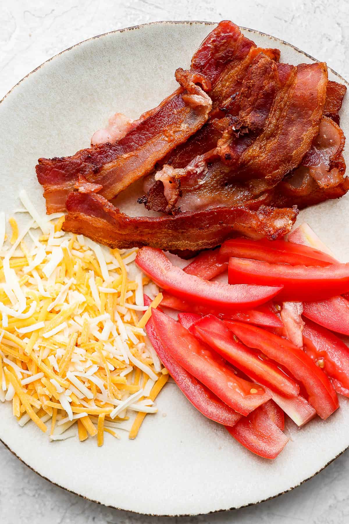 Bacon, tomatoes, and shredded cheese on a plate.