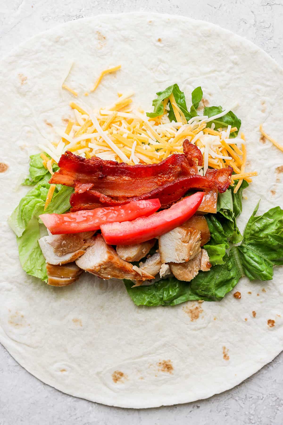 Chicken bacon ranch filling ingredients down the middle of a large tortilla.
