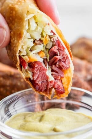 Someone dipping a corned beef and cabbage egg roll into some dijon mustard.