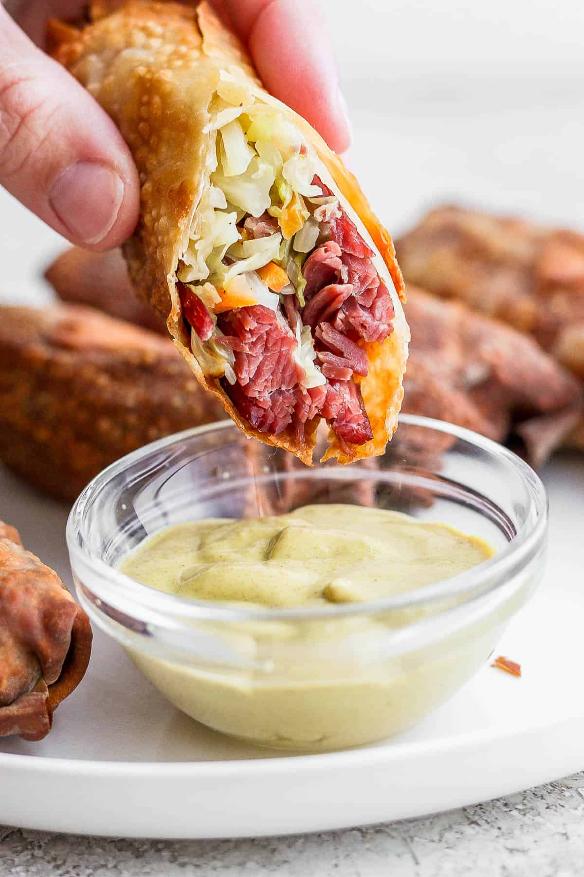 A corned beef and cabbage egg roll being dipped in a small dish of dijon mustard.