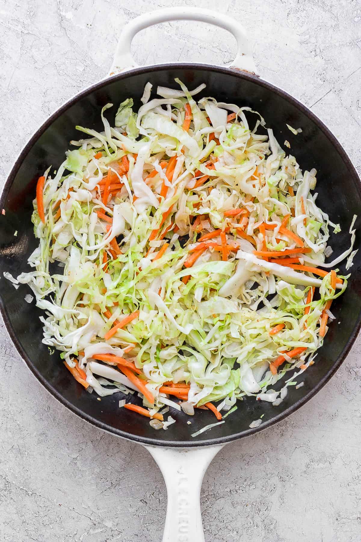 Shredded onion, cabbage, carrots, and minced garlic in a cast iron skillet.