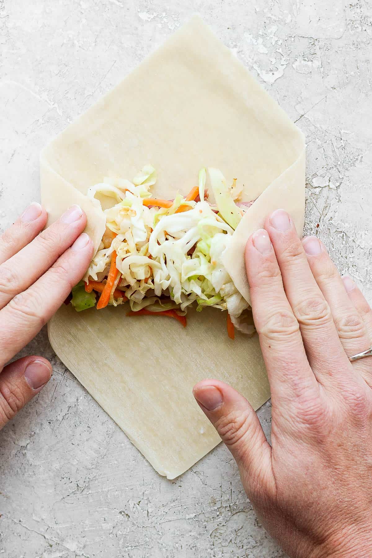 Two hands folding in the sides of the egg roll wrapper.