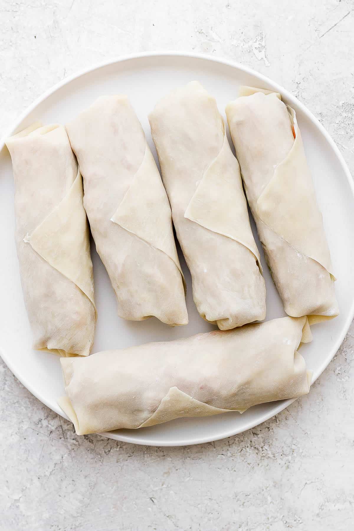 Egg rolls on a white plate before they have been cookied.