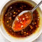 A bowl of hot honey sauce with a spoon lifting up some closer to the camera.