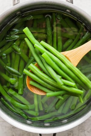 A saucepan of boiled green beans with a wooden spoon lifting a few out.