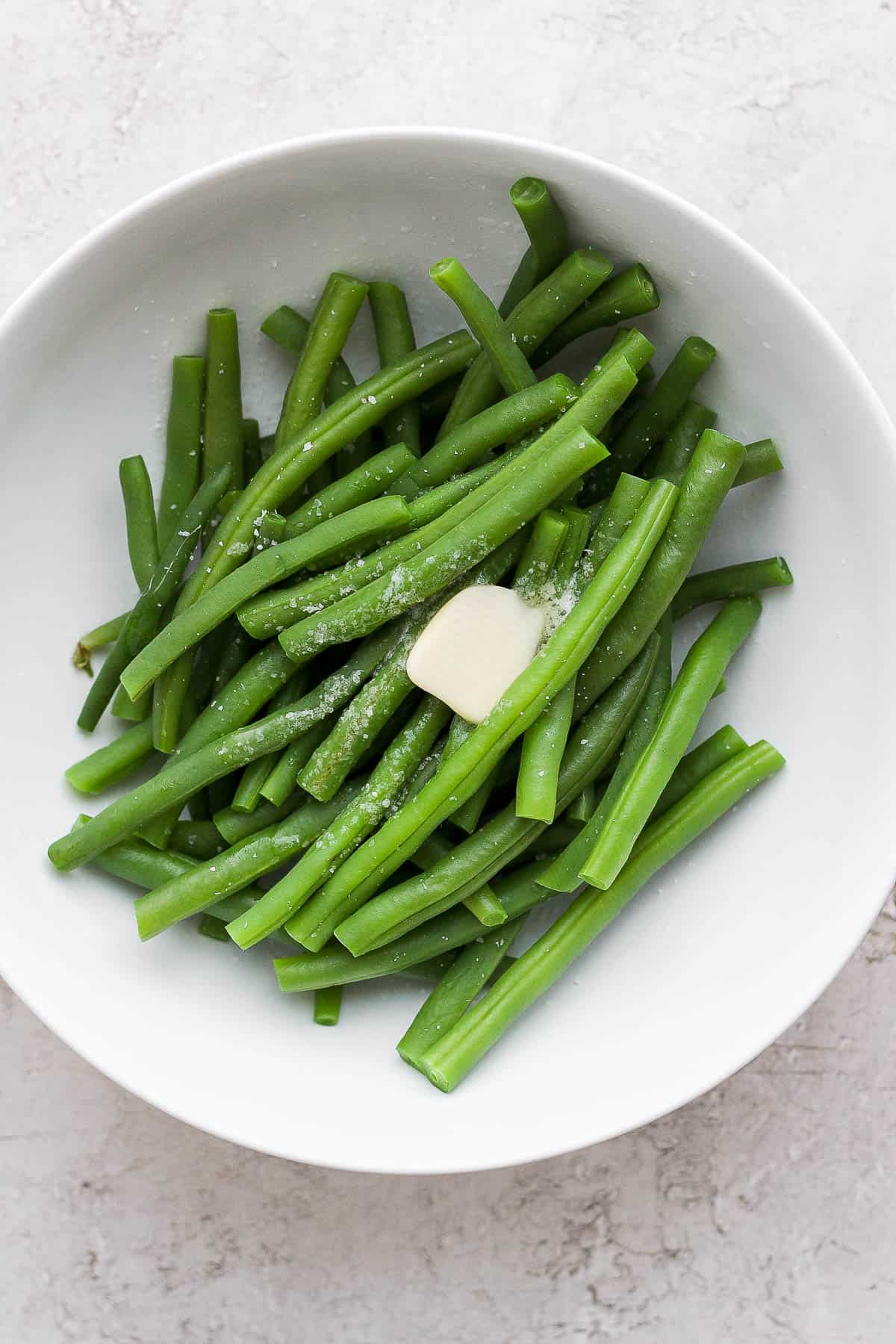 Boiled green beans on a plate topped with a pat of butter and sprinkled with salt.