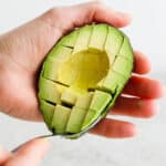 Someone holding an avocado half and cutting into cubes.