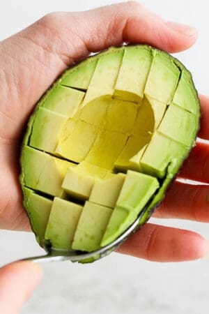 Someone holding an avocado half and cutting into cubes.
