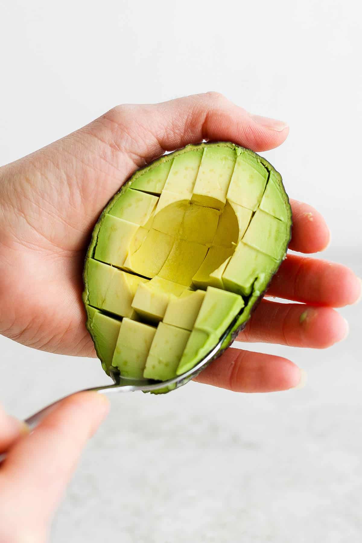 A spoon scooping a diced avocado out of the skin.