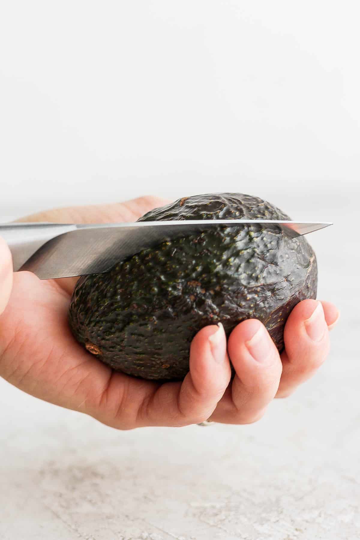 A hand holding an avocado and a knife down the middle.