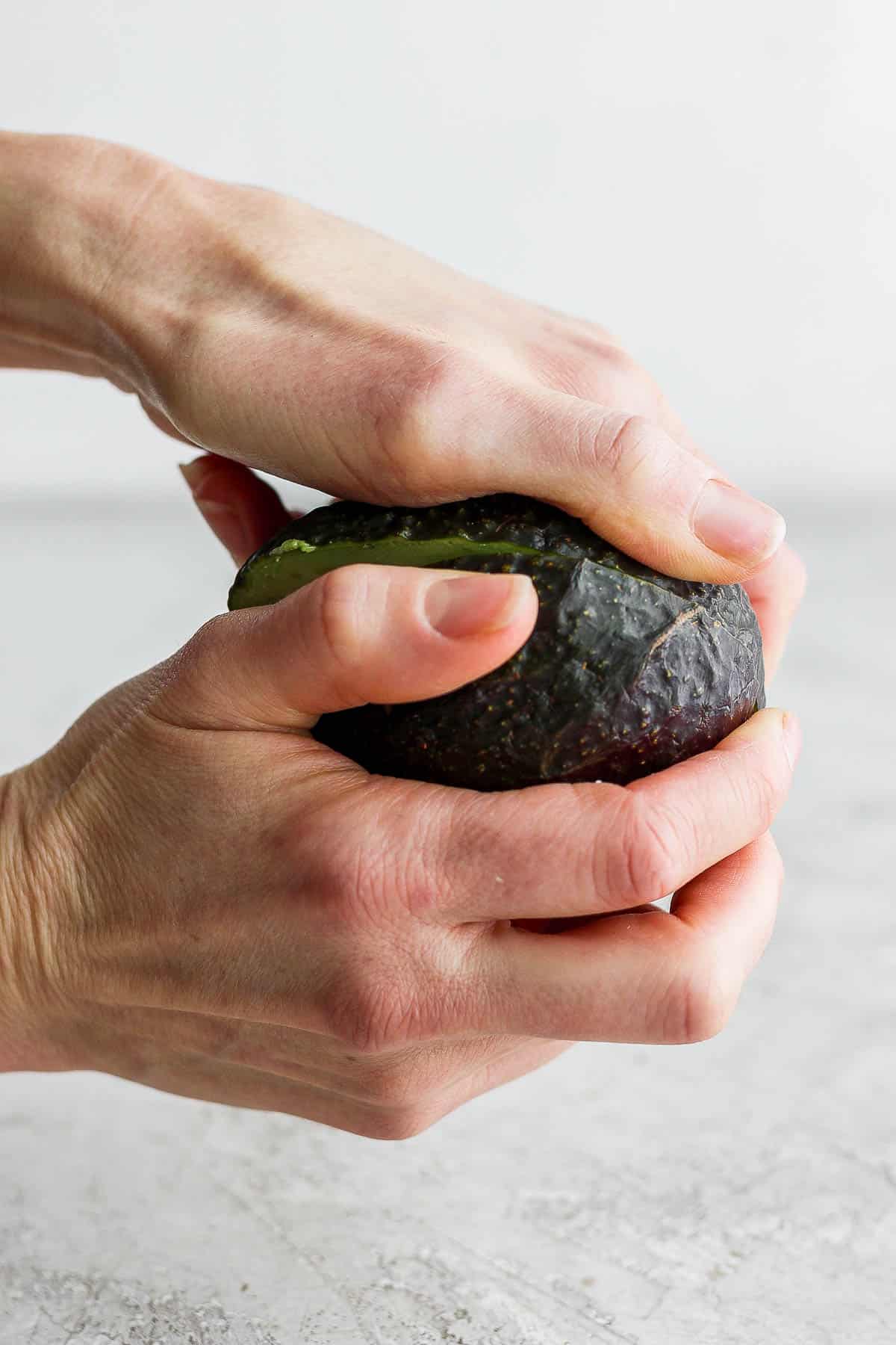 Two hand twisting an avocado into two halves.