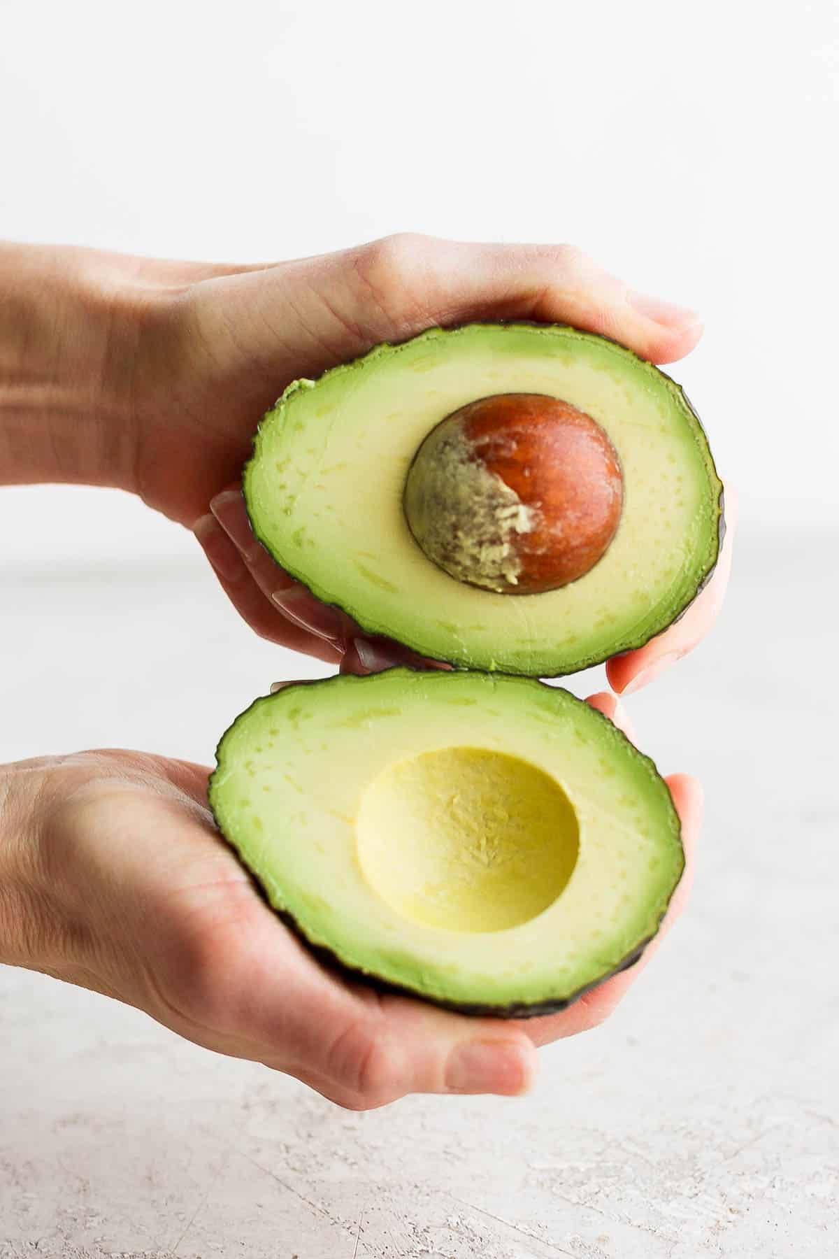 Hands holding both halves of an avocado.