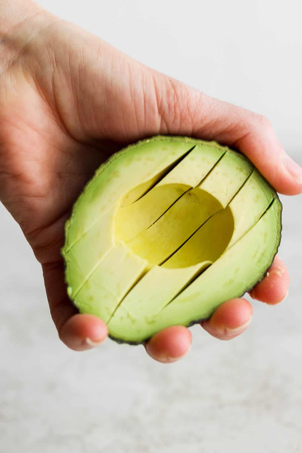 A hand holding half of an avocado that's been sliced.