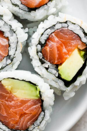 A close up of three pieces of a spicy salmon roll with avocado.