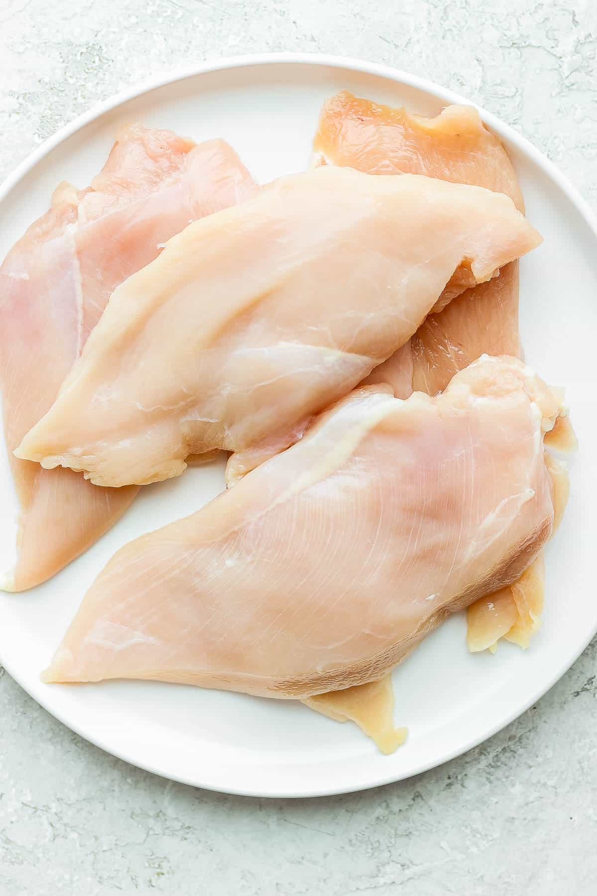 Raw chicken cutlets on a white plate.