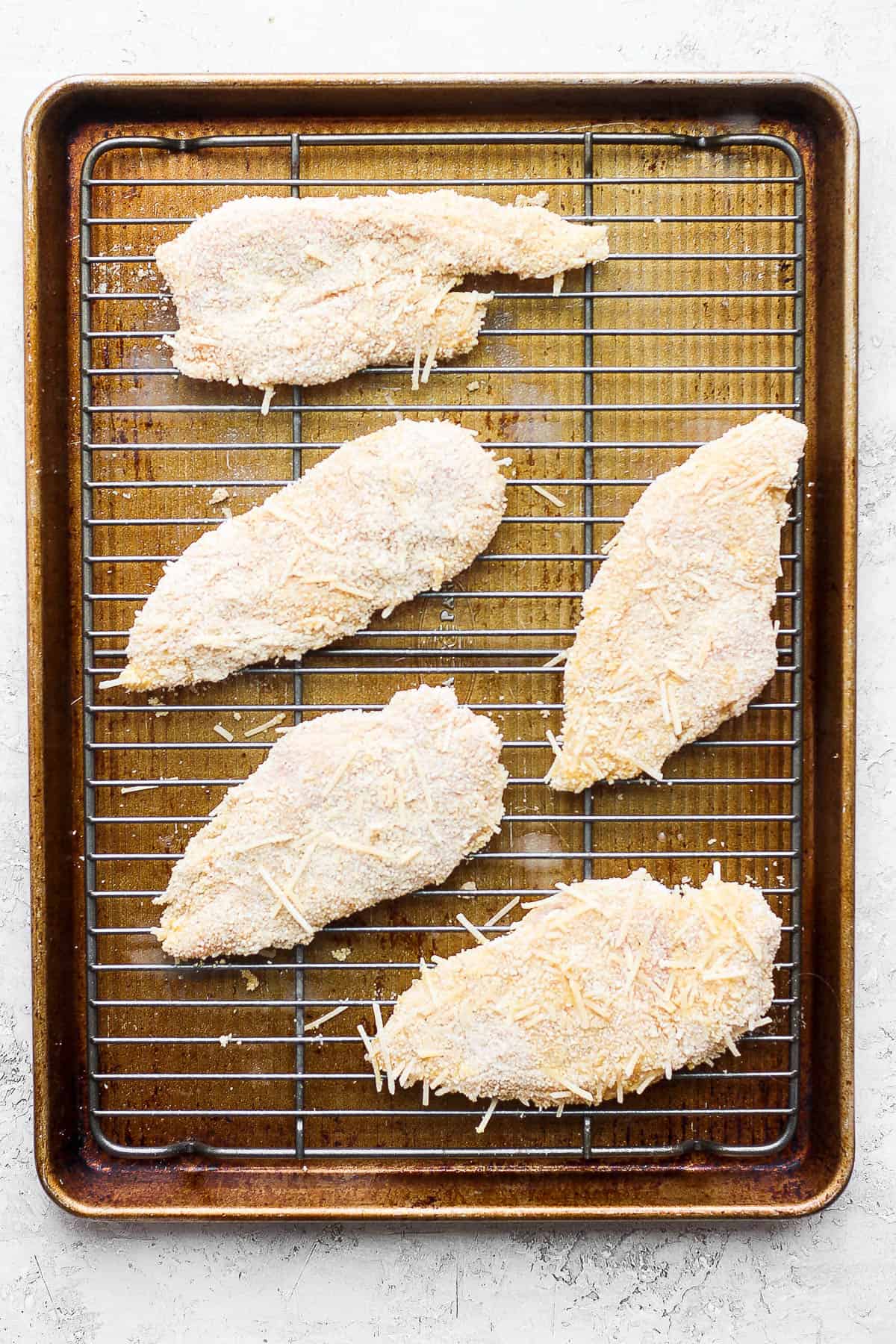 Fully coated chicken cutlets on a wire rack on a baking sheet.