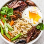 Bowl of Beef Ramen with mushrooms, green onion, carrot and a poached egg.