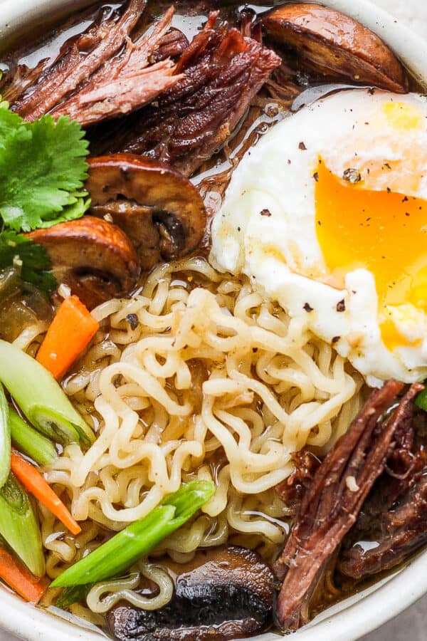 Bowl of Beef Ramen with mushrooms, green onion, carrot and a poached egg.