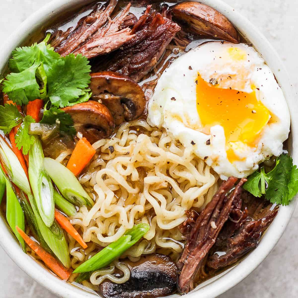Bowl of Beef Ramen with mushrooms, green onion, carrot and a poached egg.