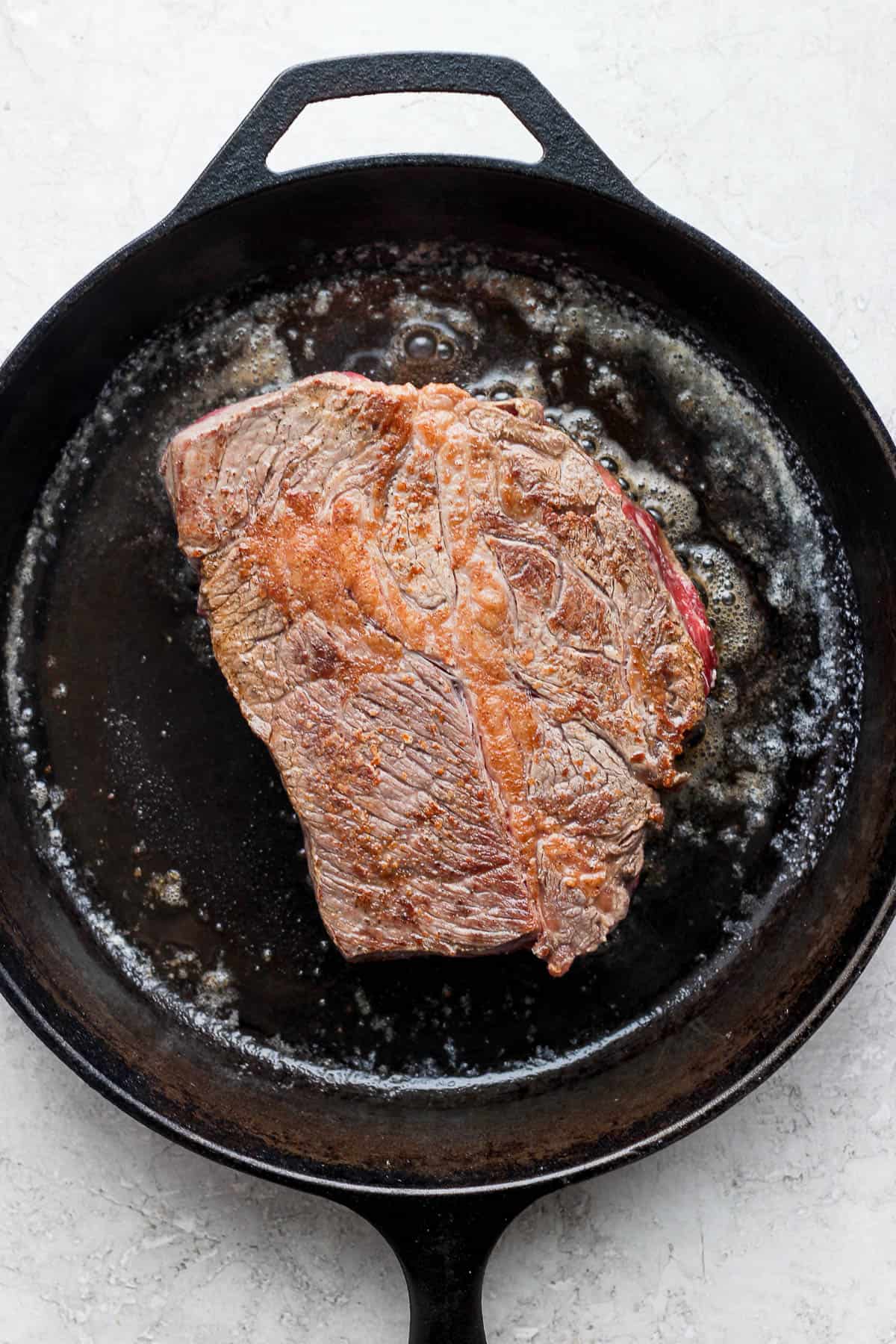 The seasoned chuck roast being seared in a cast iron skillet.