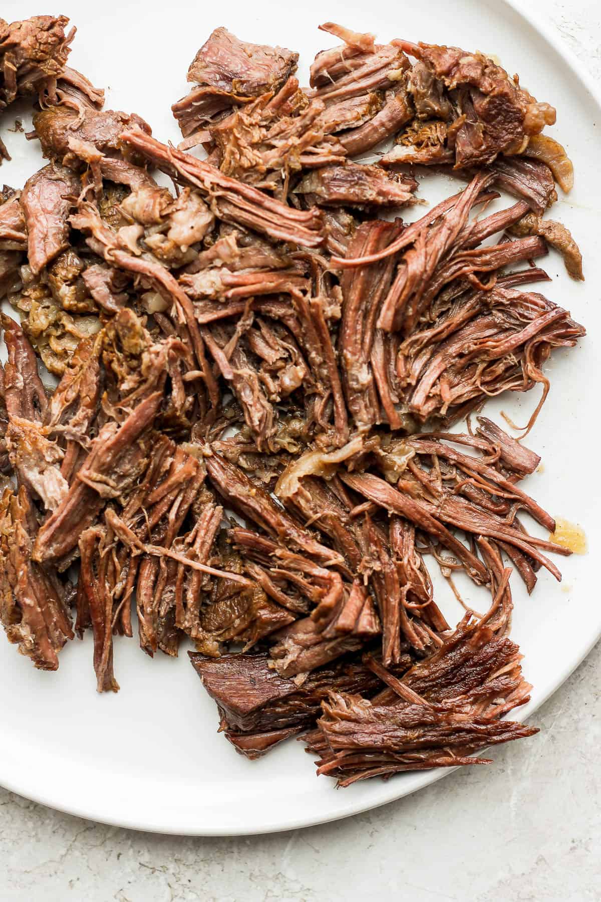 The beef removed from the slow cooker and shredded on a plate.