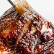 A close-up of a brush adding brown sugar ham glaze to the top of a cooked ham.