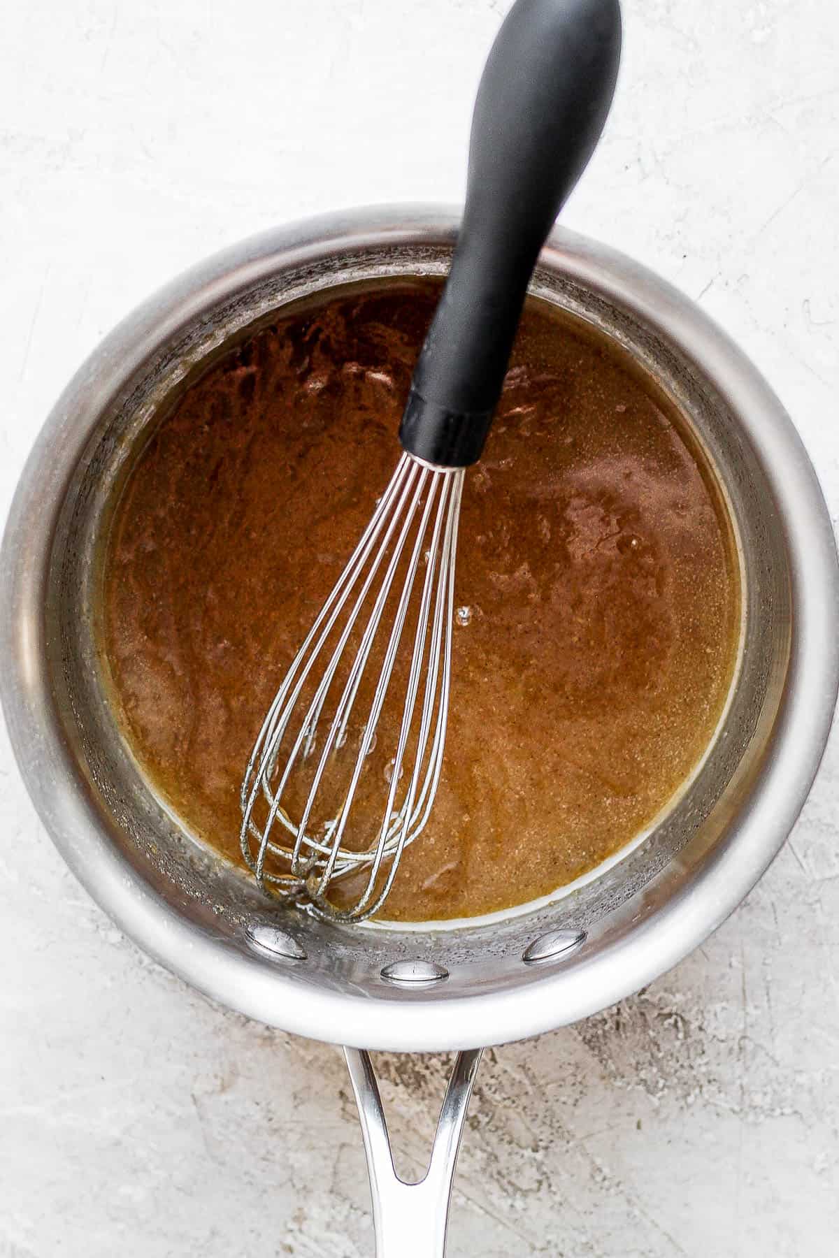 Brown sugar ham glaze in a saucepan with a whisk.