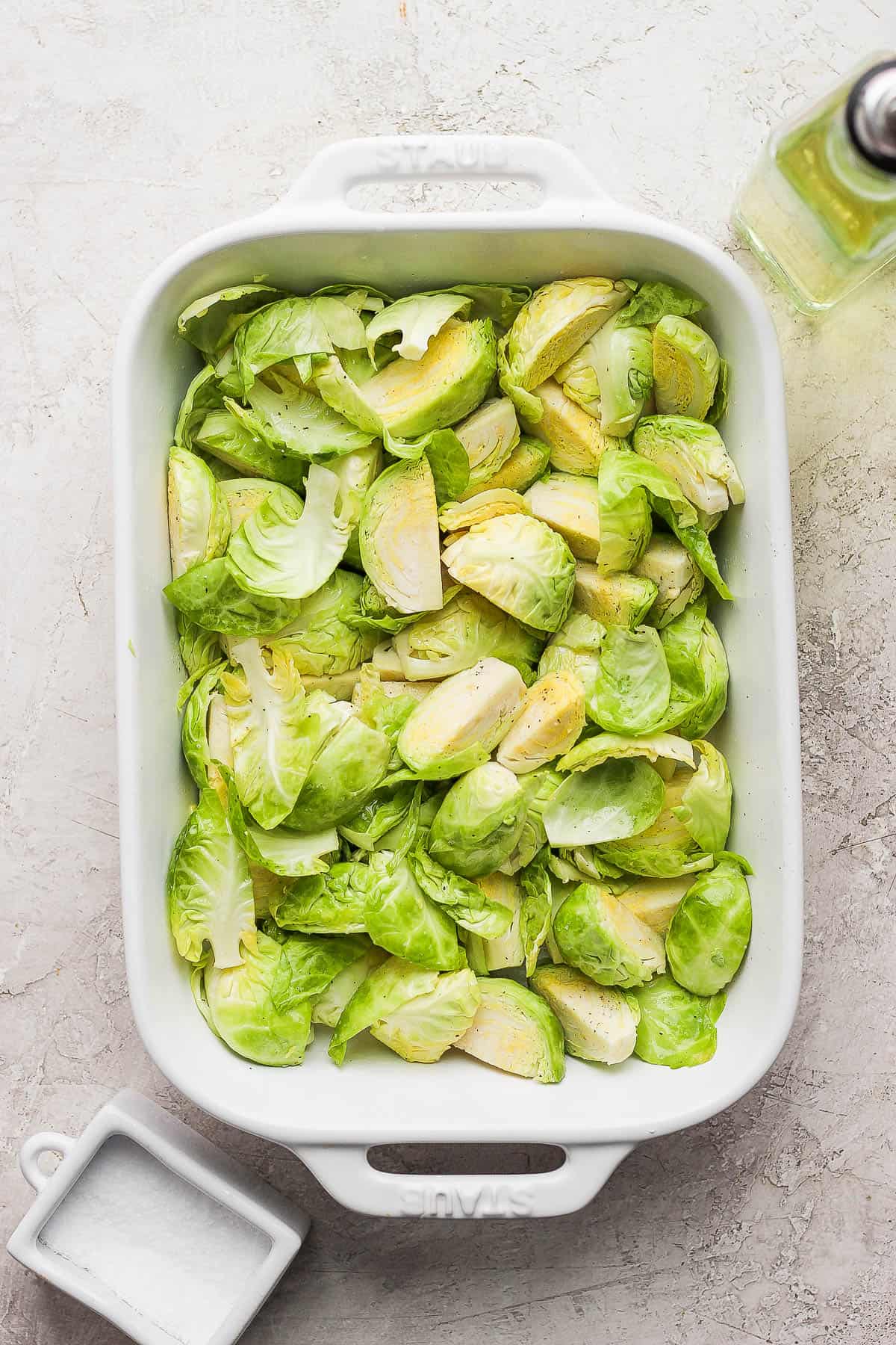 Peeled and quartered brussels sprouts in a casserole dish drizzled with olive oil and salt and pepper.
