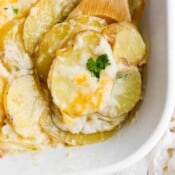 Top shot of the corner of a casserole dish of scheesy scalloped potatoes with a spoon under a small chunk.