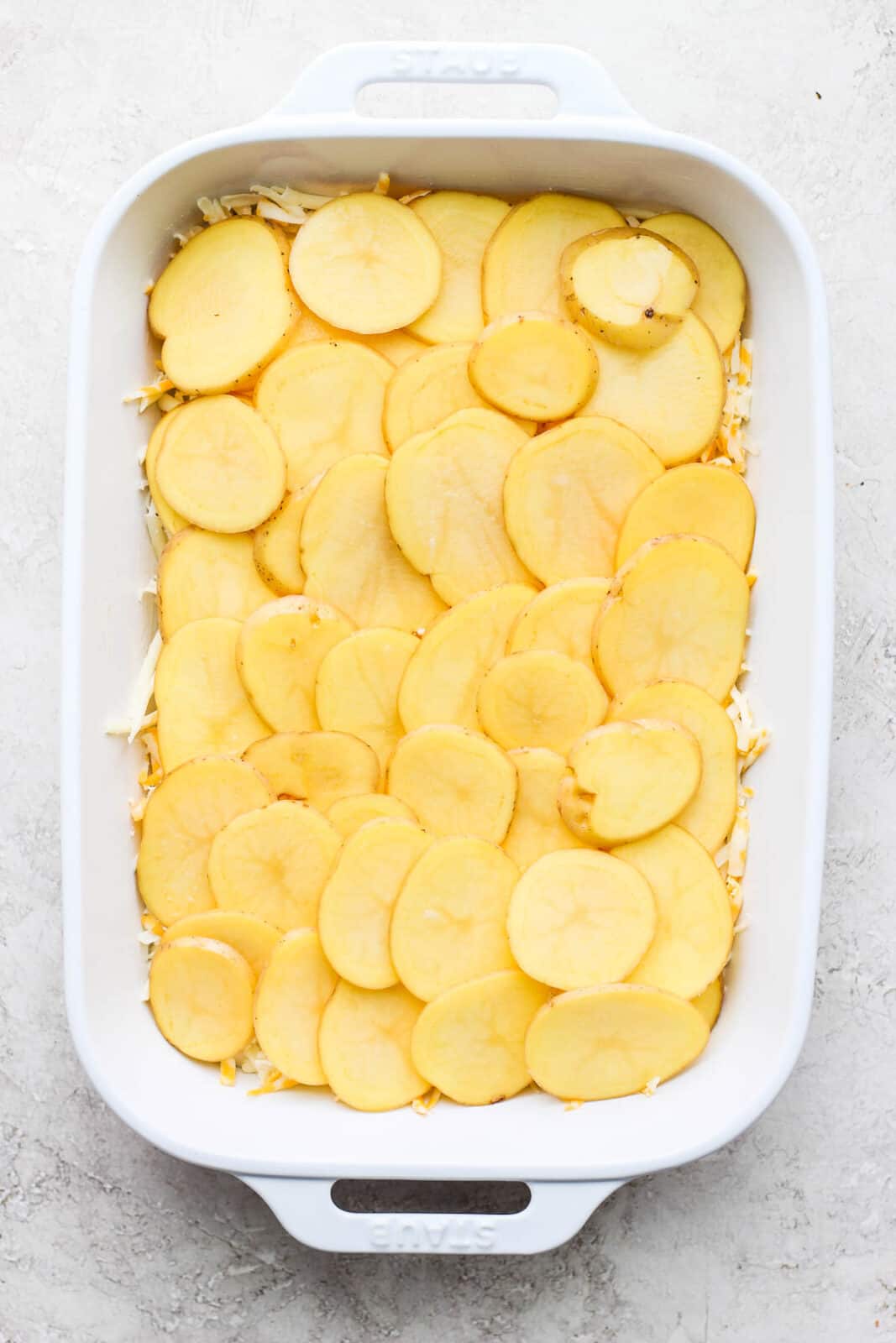 Another layer of potato slices added on top of the shredded cheese.