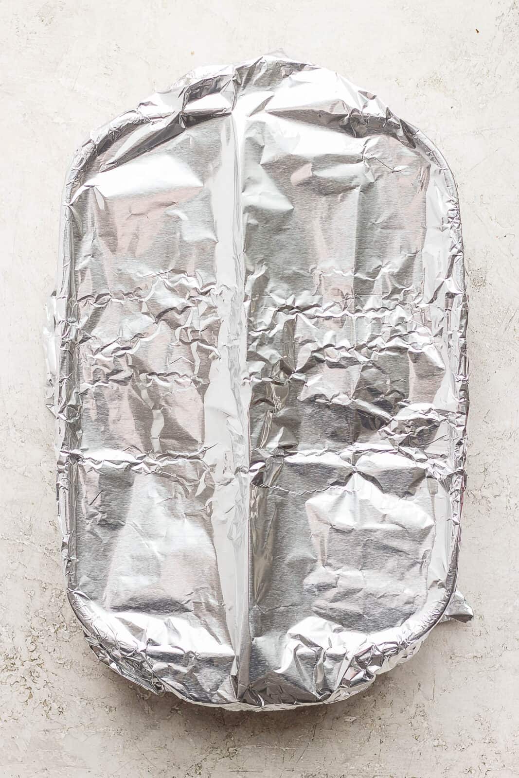 Casserole dish of unbaked cheesy scalloped potatoes covered with aluminum foil.