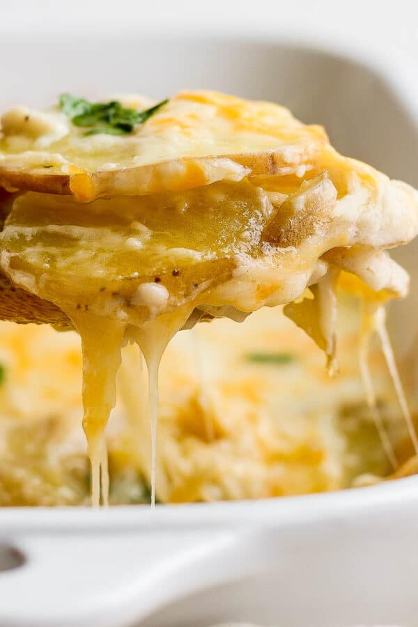 A wooden spoon lifting out a few layer of cheesy scalloped potatoes from a casserole dish.