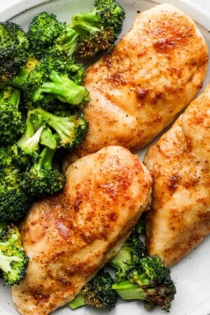 A close up of a plate of air fryer chicken breasts on a plate with seasoning and broccoli next to them.