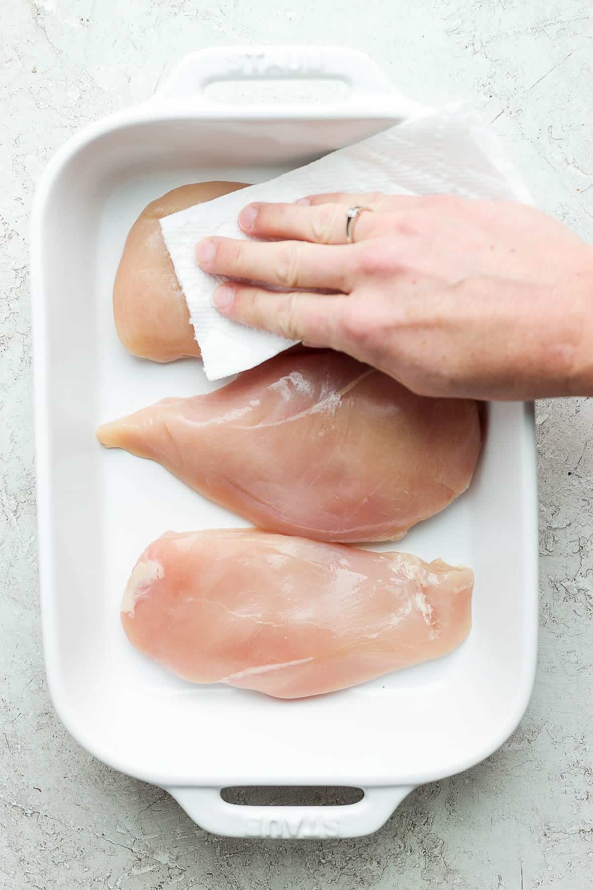 Raw chicken breasts being pat dry with paper towel.