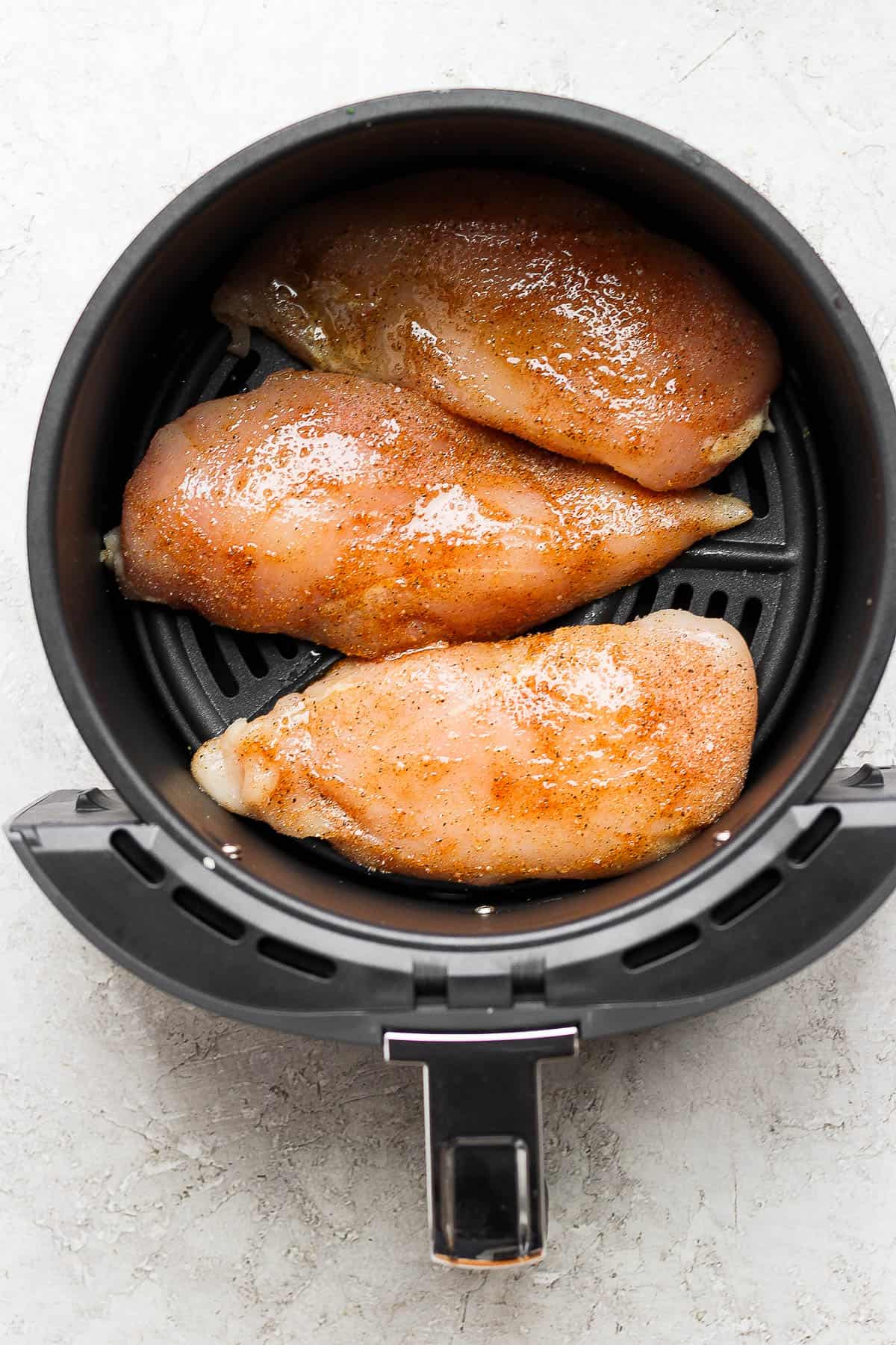 Seasoned chicken breasts in the air fryer basket.