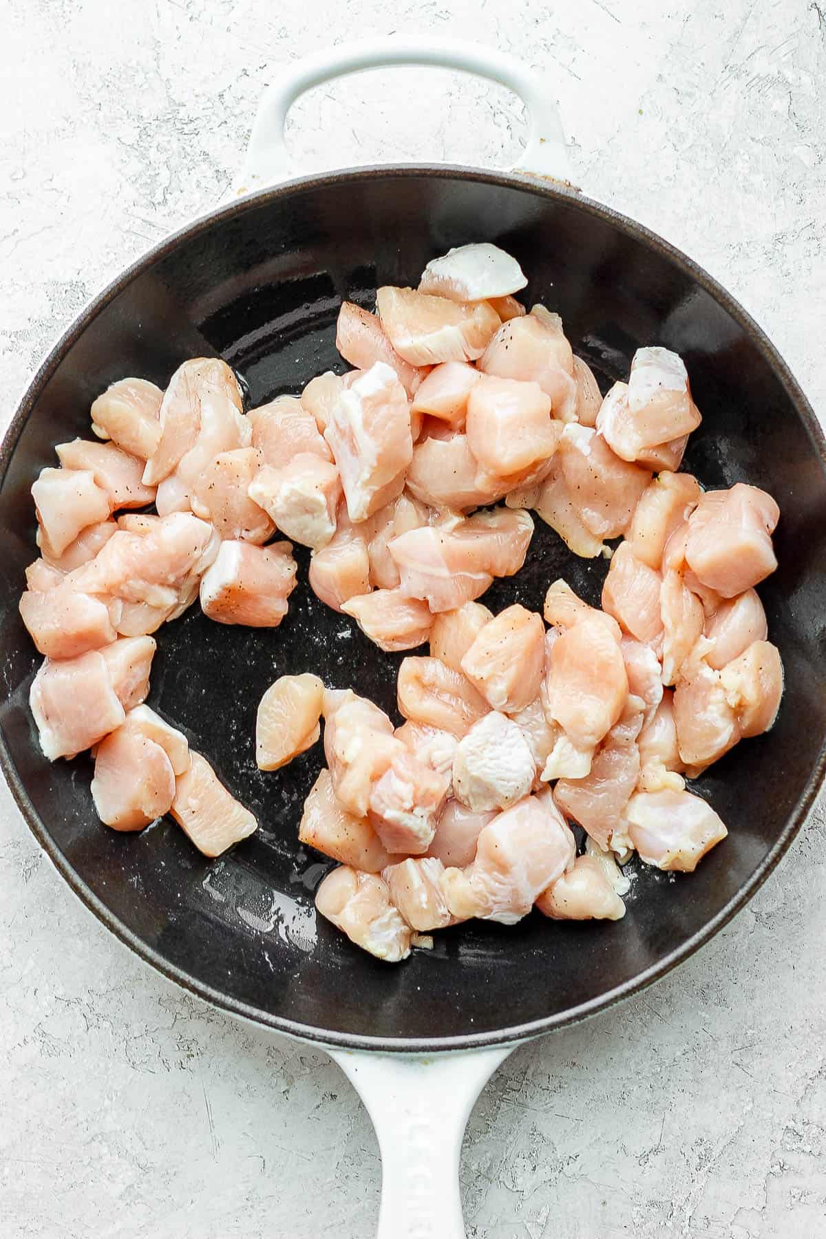 Chunks of raw chicken in a skillet.