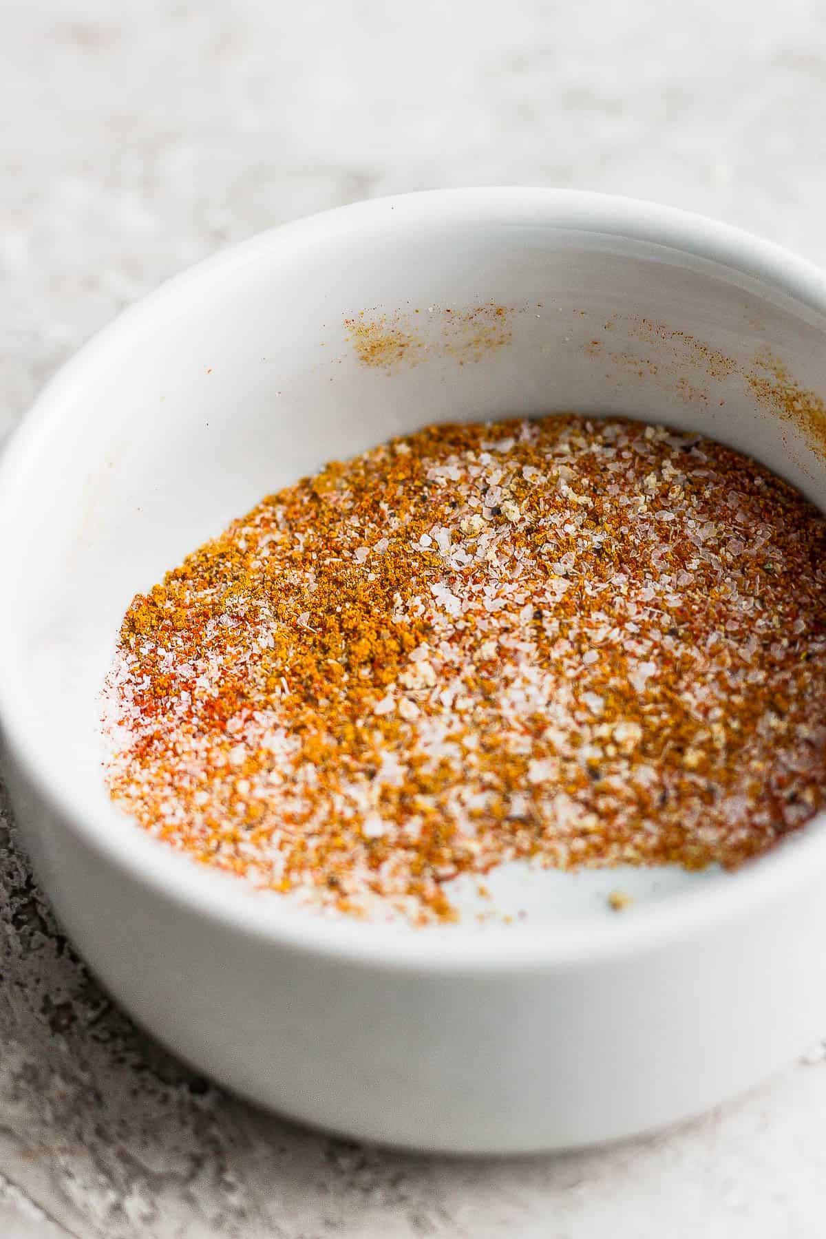 A smal pinch bowl with curry powder, salt, ground black pepper, paprika, onion powder, and garlic powder mixed together.