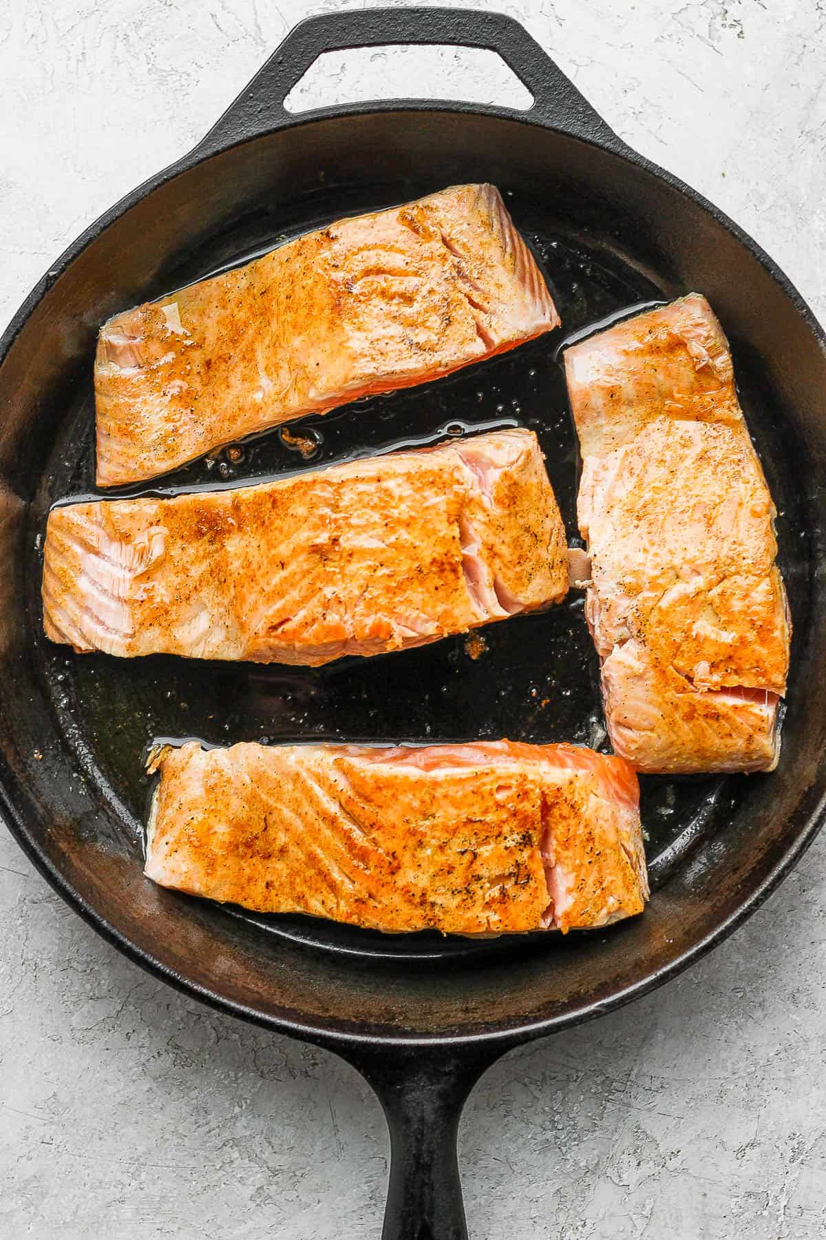 Four salmon filets in a cast iron skillet being seared.