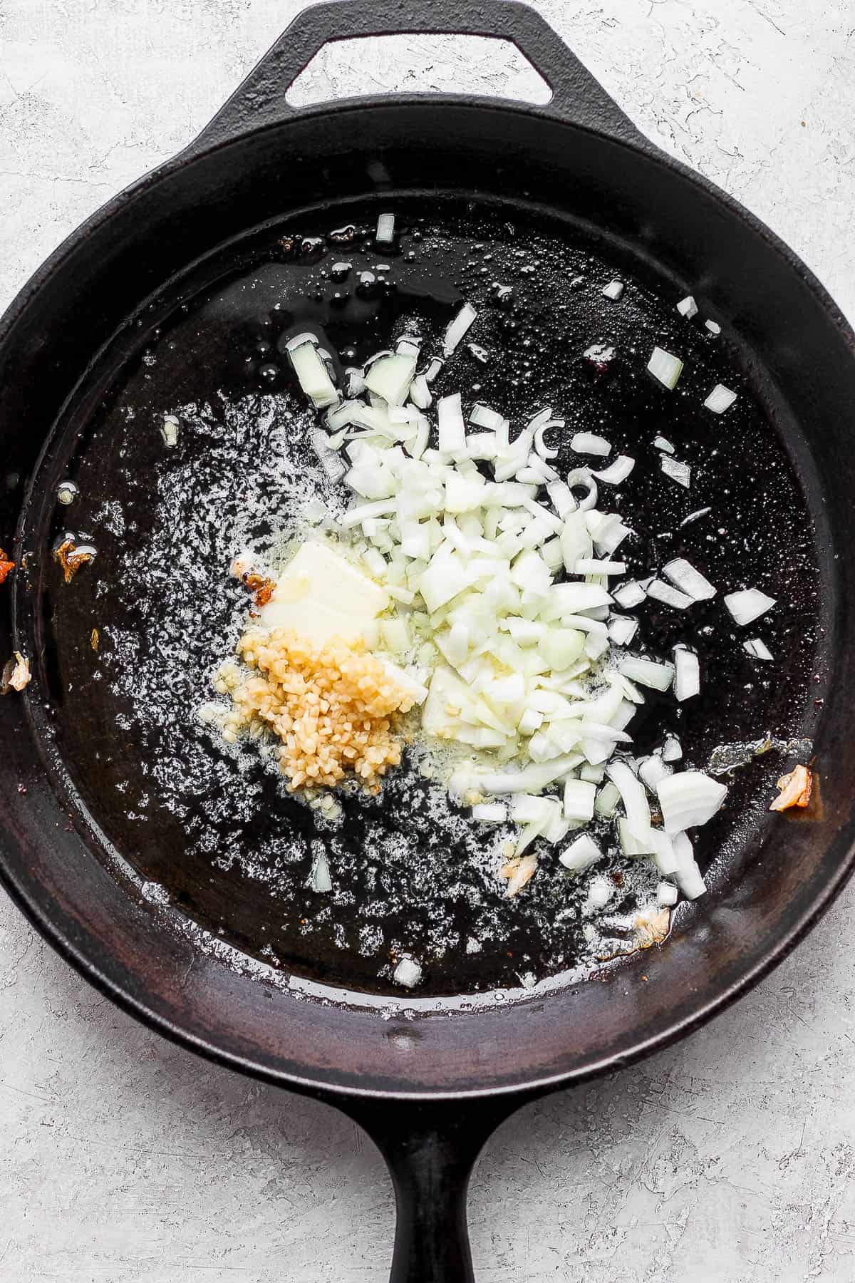 A cast iron skillet with a pat of butter, minced garlic, and chopped onion.