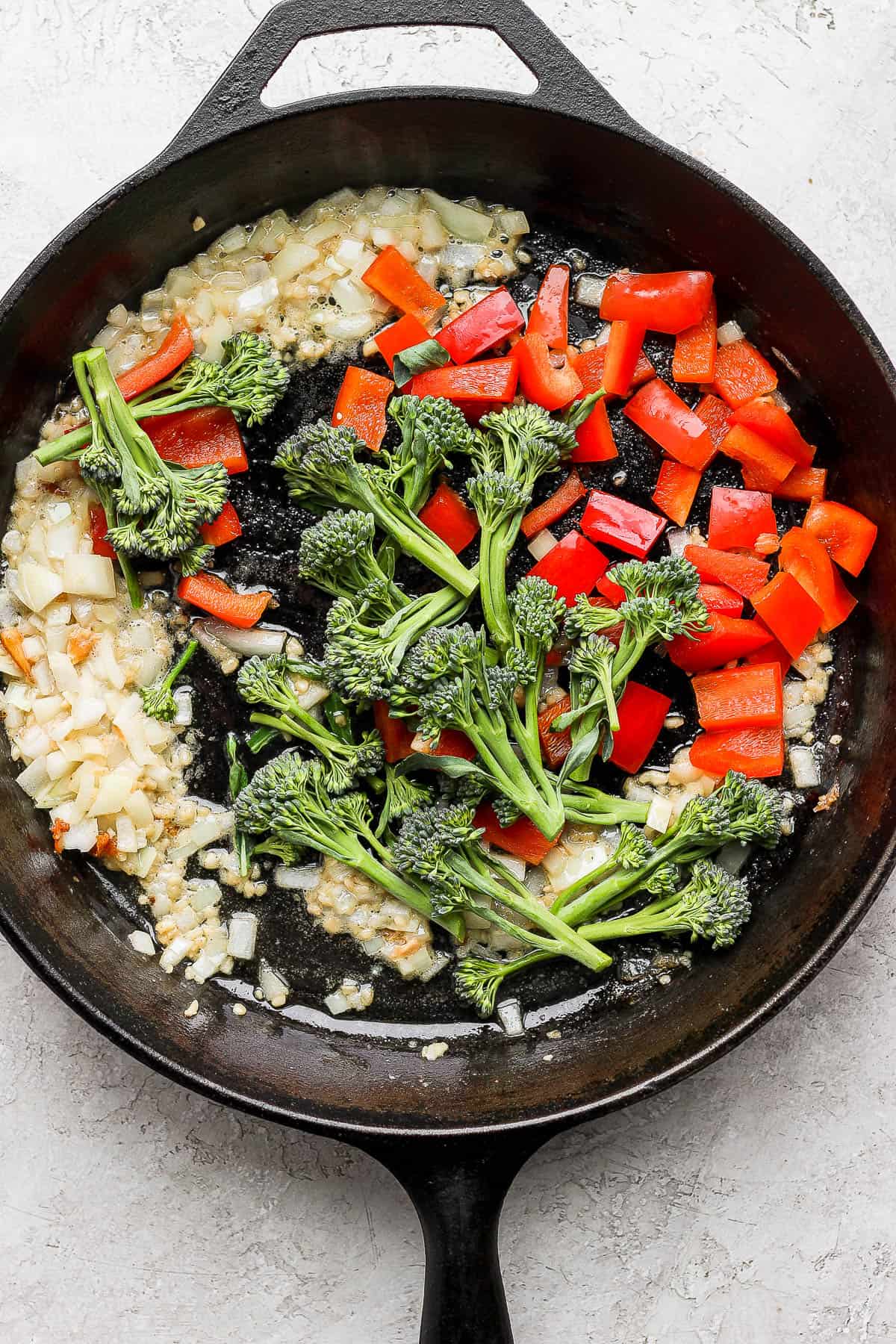 Broccoli and chopped red bell pepper added to the cast iron skillet.
