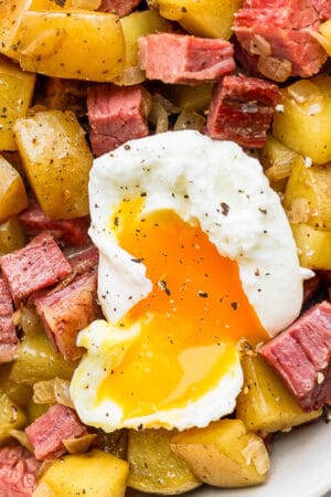 An up close shot of a bowl of corned beef hash with a poached egg on top.