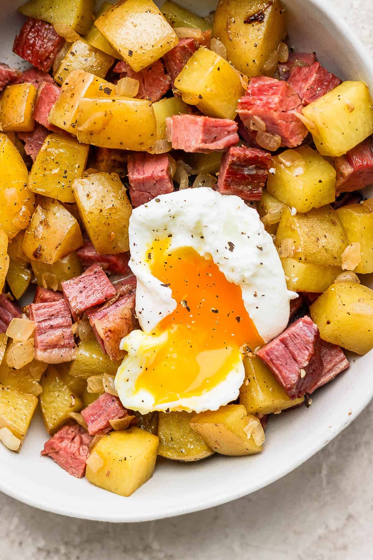 Corned Beef hash in a bowl topped with a poached egg and fresh cracked pepper.